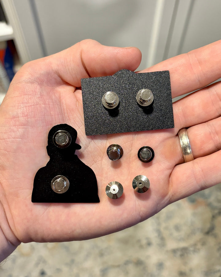 Magnetic pin backings held in hand with enamel pins