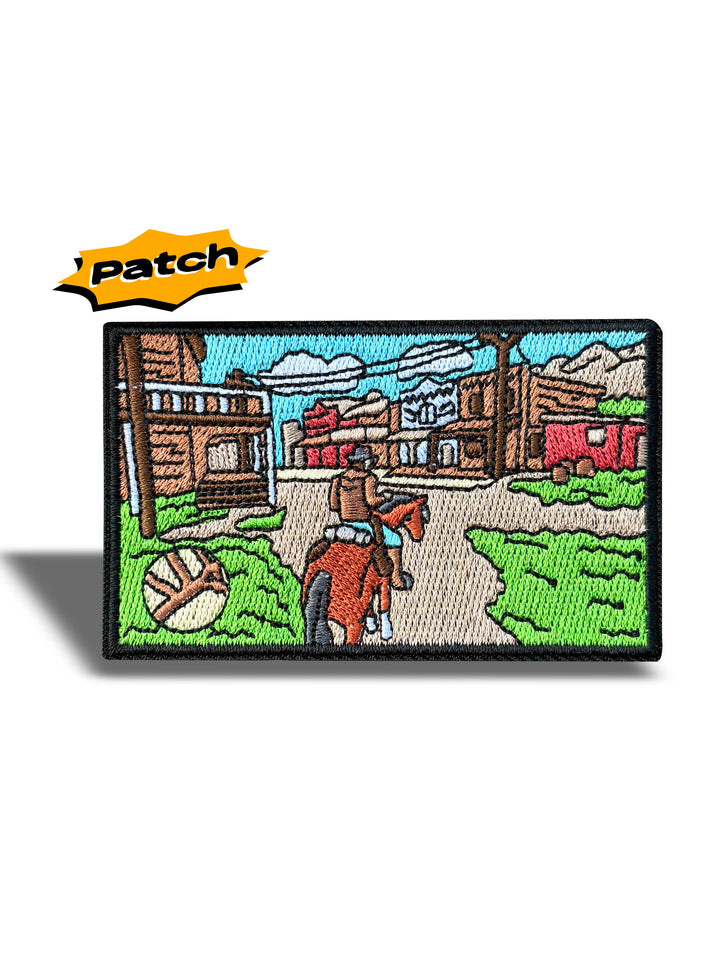 An embroidered rectangular patch featuring a western town street scene with a cowboy on a horse, wooden buildings, mountains, and a blue sky. A yellow 'Patch' logo appears above the patch on a white background.