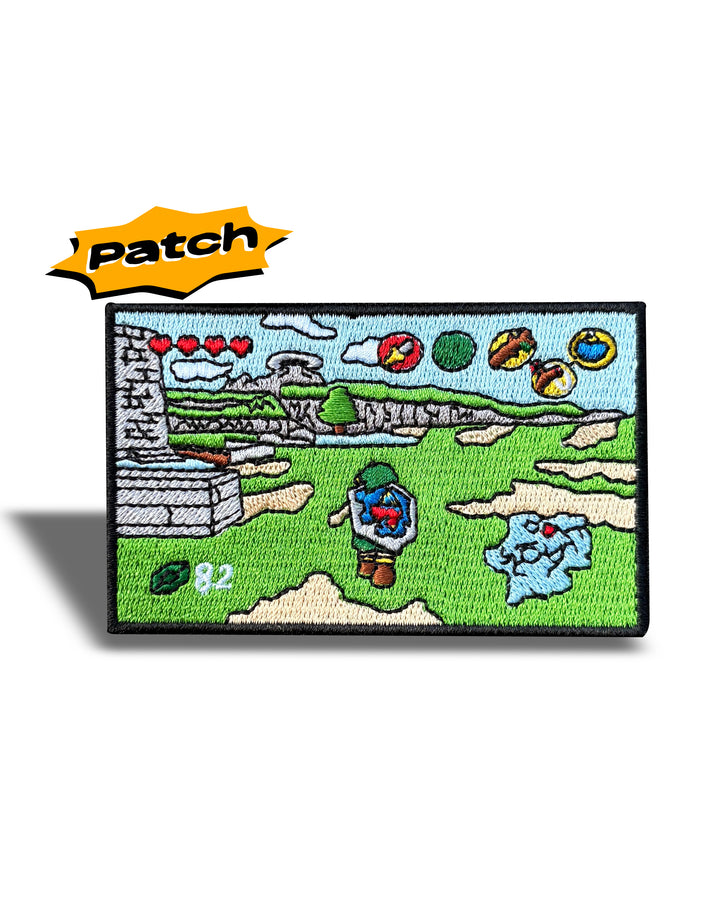 A rectangular embroidered patch featuring a pixel-art landscape scene with green grass, gray stone walls, blue sky, and small colorful icons, shown on a white background with an orange 'Patch' label above it.